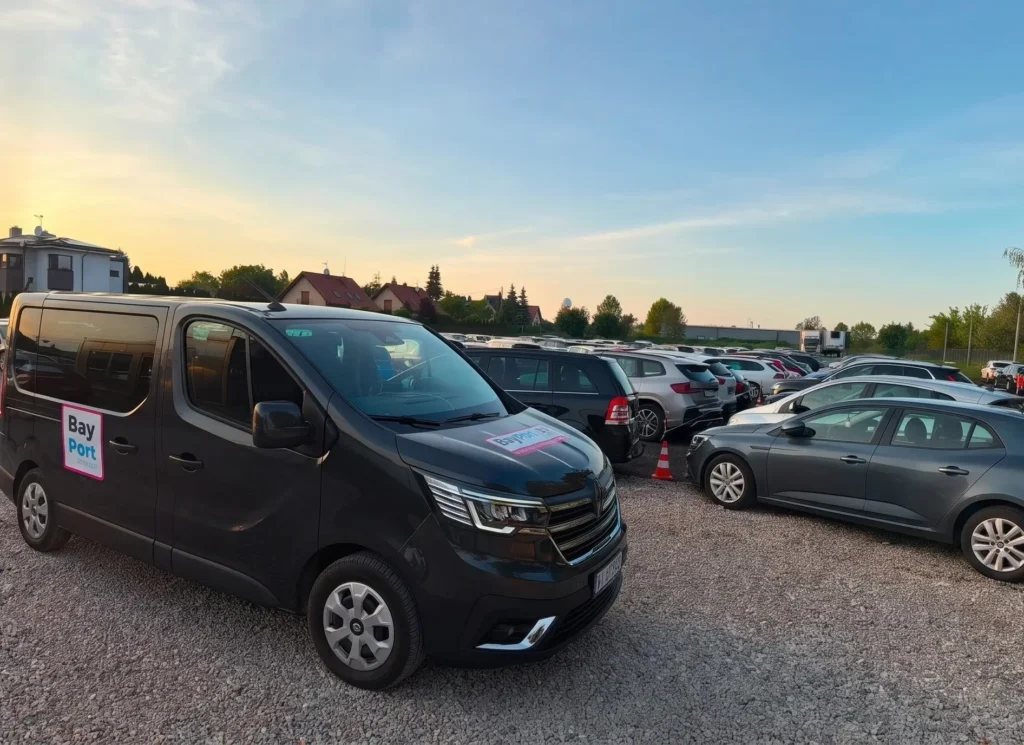 Czarny bus BayPort zaparkowany na parkingu przy Lotnisku Chopina w Warszawie, w otoczeniu samochodów osobowych.